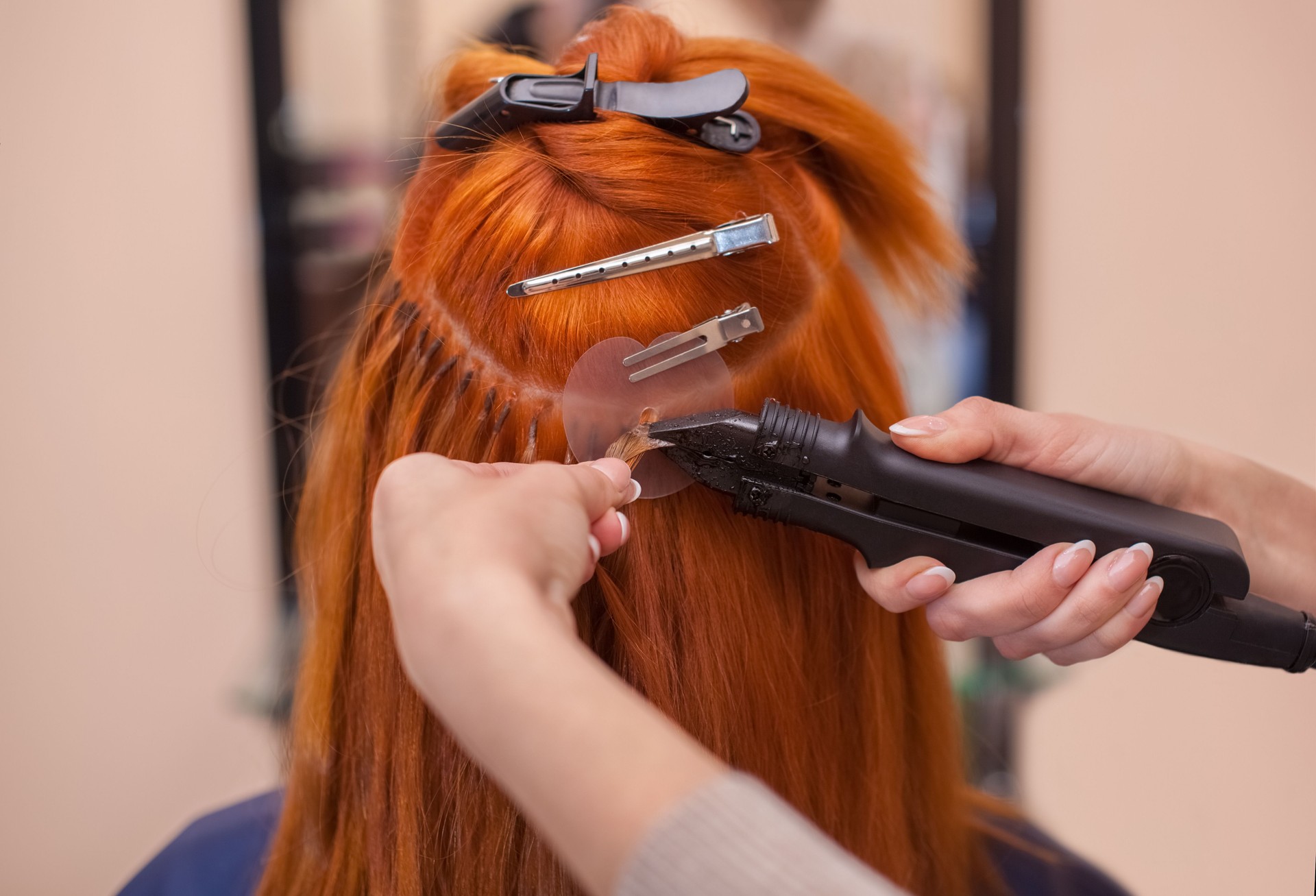 hairdresser does hair extensions to a young, red-haired girl, in a beauty salon