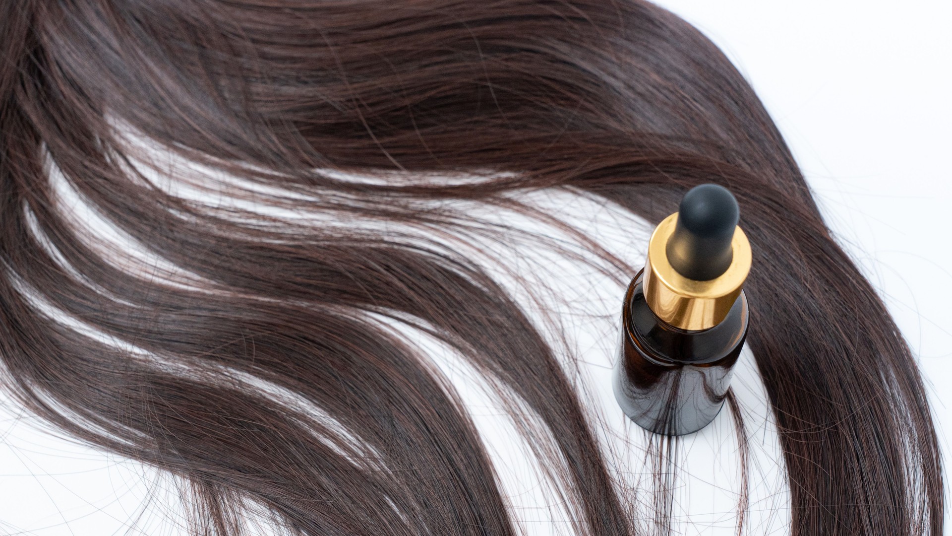 Luxurious hair serum bottle placed elegantly beside flowing strands of dark hair, showcasing beauty and hair care essentials for healthy locks